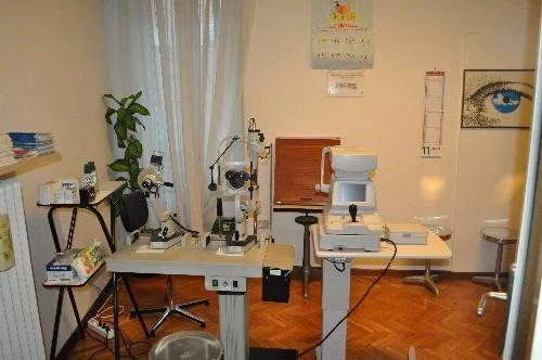 L'ambulatorio oculistico della sede: una lampada a fessura e un autorefrattometro su due tavoli, davanti a una finestra con le tende; alla parete un quadro con un grande occhio azzurro.